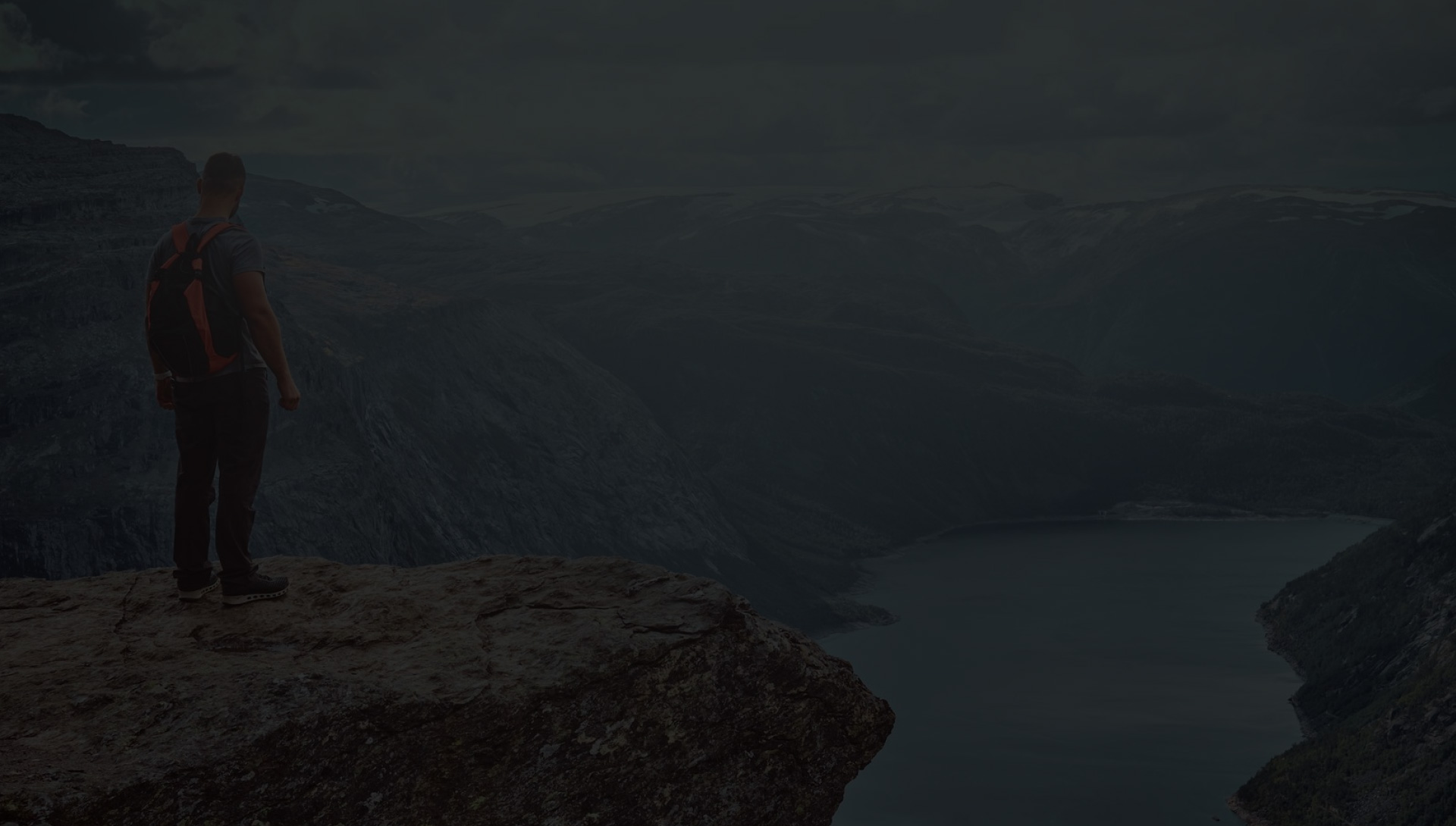 man stood on mountain edge overlooking lake